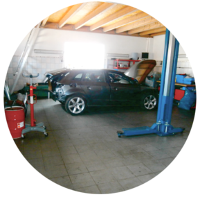Ein Auto mit offenem Motorraum steht hinter der blauen Hebebühne in der Werkstatt.